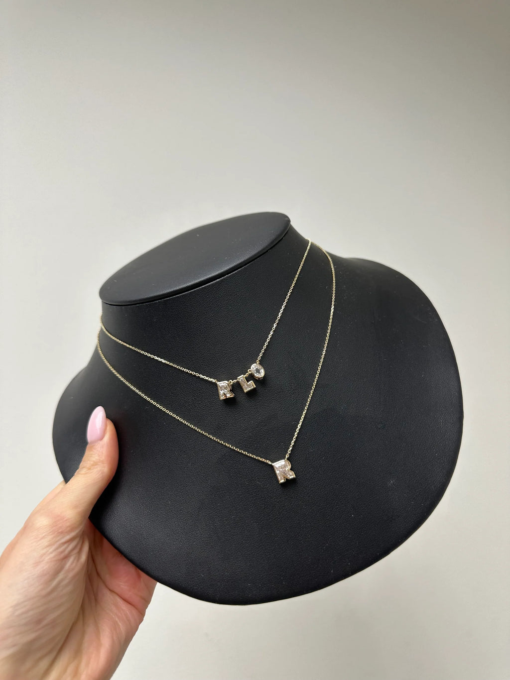 Gold necklace with three pendant drops on a black jewelry display stand, held by a hand against a plain background.