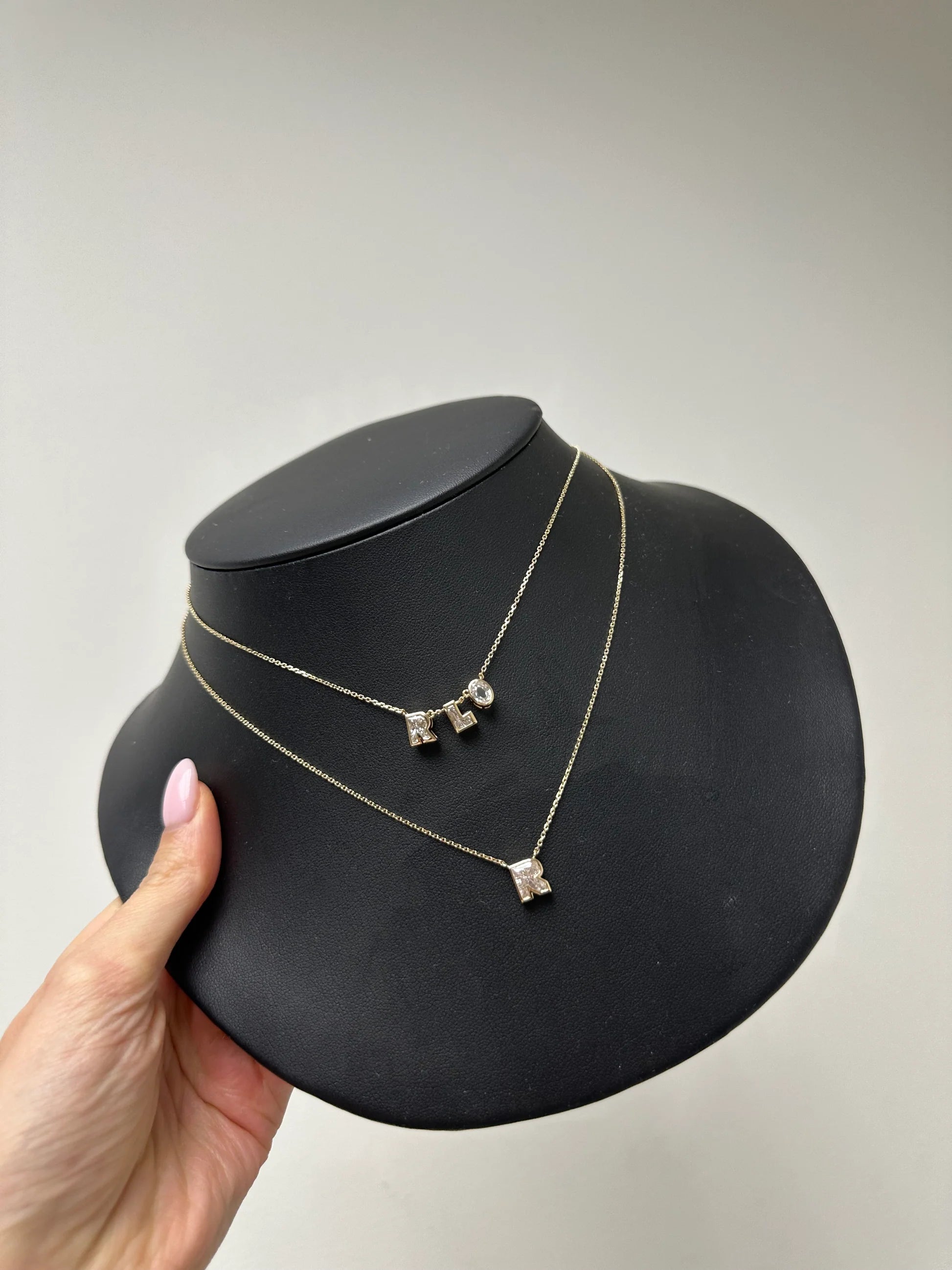 Gold necklace with three pendant drops on a black jewelry display stand, held by a hand against a plain background.
