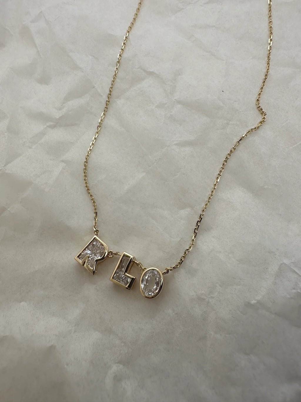Gold necklace with 'RLO' pendant on a marble surface