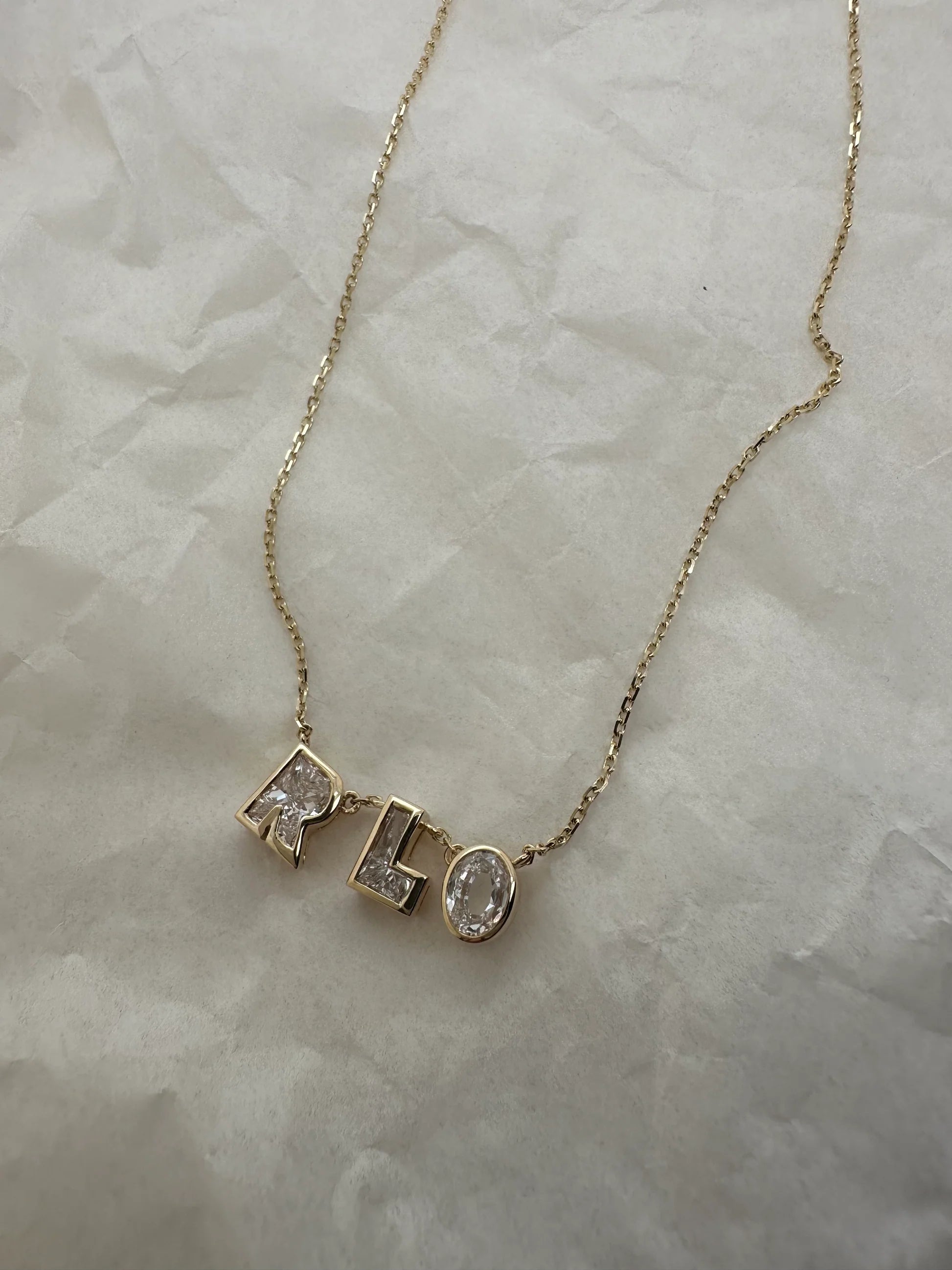 Gold necklace with 'RLO' pendant on a marble surface