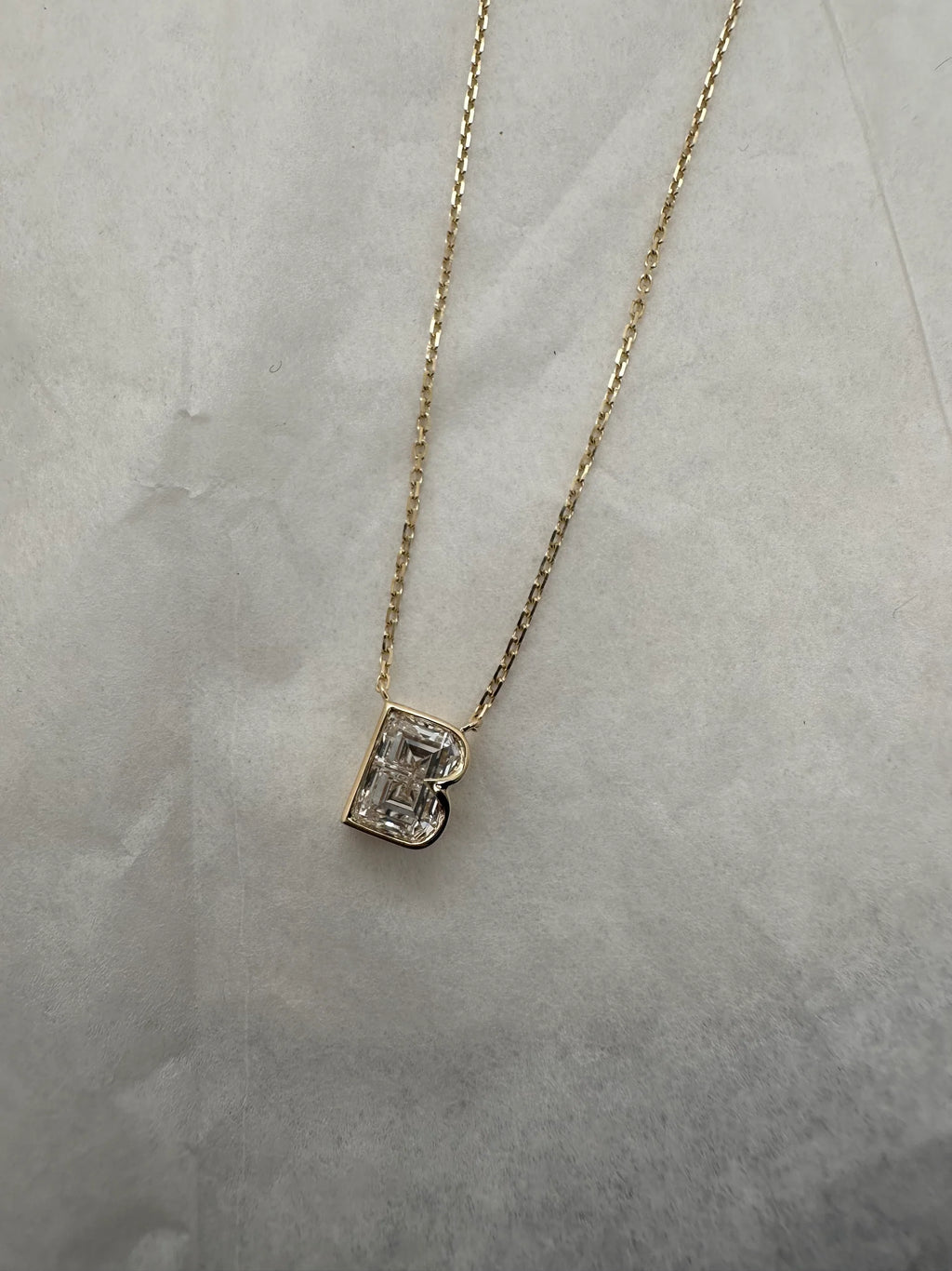 Gold necklace with a letter 'B' pendant on a light gray background